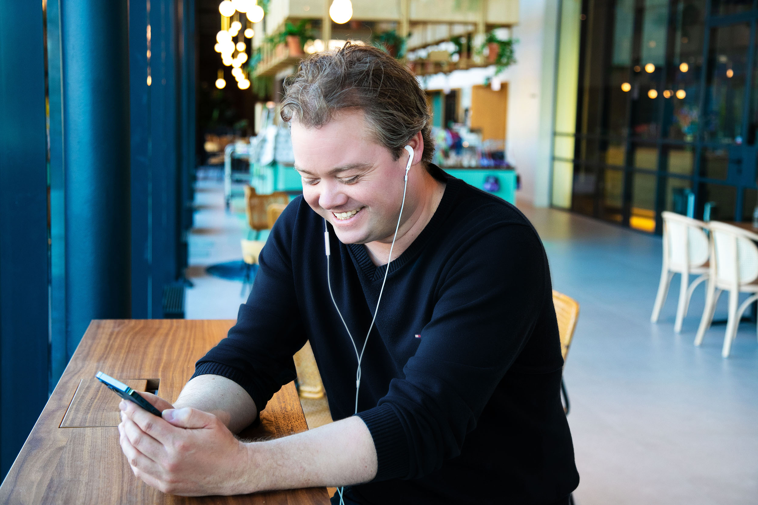 Man die lachend naar zijn mobiel kijkt met koptelefoon